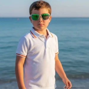 Niño con polo blanco y bandera de España frente al mar